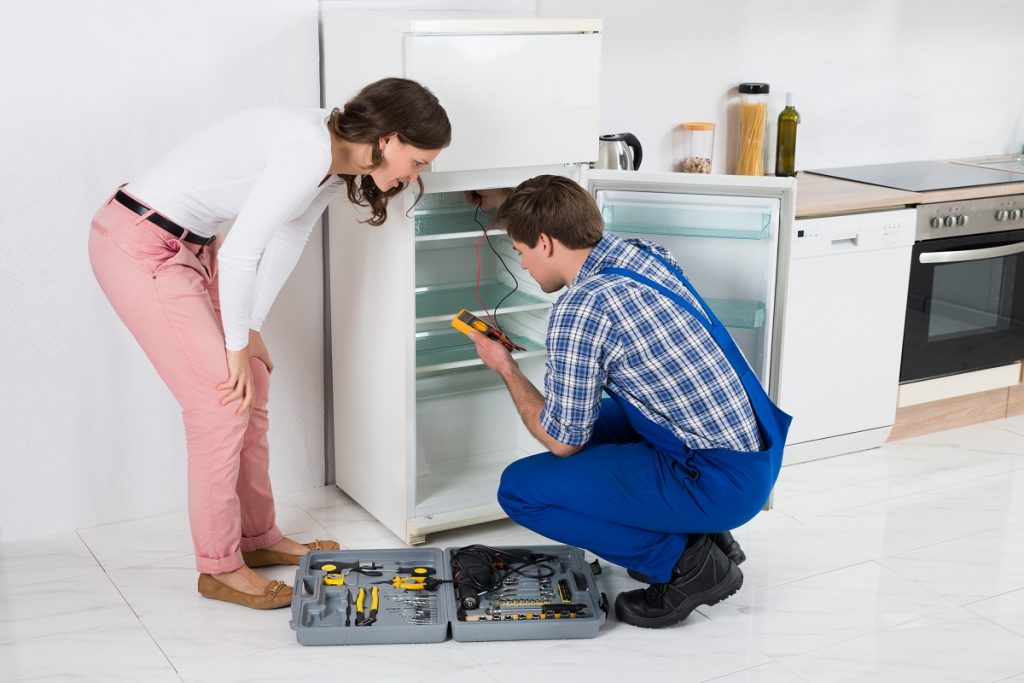 Woman watching man repair fridge