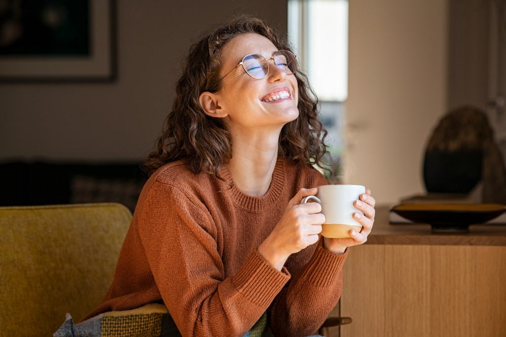 Smiling, young woman having a cup of coffee while sitting in the living room of her home.